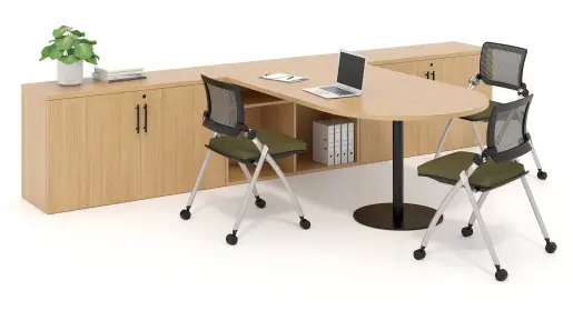Modern light wood collaboration table on a black pedestal base, attached to a long matching credenza storage unit, and green folding chairs on casters, a laptop, binders, and a potted plant accessorize the meeting area against a clean white background. Versatile solution for dynamic workspaces from Office Furniture Connection's selection of office tables in Houston TX.
