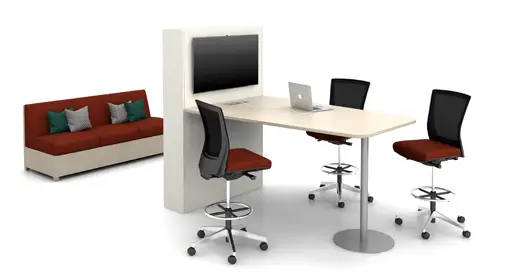 Modern workspace featuring a AIS Day to Day Collab bar height light-colored media table with pedestal base, attached to a panel with integrated monitor mount, laptop setup, three adjustable mesh-back stools in red upholstery, and a separate red lounge sofa with throw pillows, all against a clean white studio background. Innovative tech-friendly solution for hybrid meetings from Office Furniture Connection's selection of office tables in Houston TX.