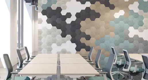 Hexagonal acoustic wall tiles in a dynamic pattern of gray, teal, beige, and white mounted behind light-wood training tables with gray mesh chairs in a sunlit open office. Perfect for noise reduction in collaborative meeting areas.