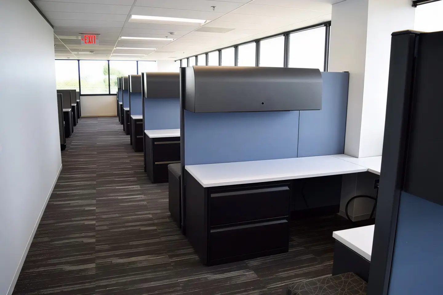 Government call center or adminstative office with rows of durable Knoll Morrison panel workstations of blue fabric, overhead storage bins, white work surfaces, black lateral files and natural light for efficient municipal employee processing and citizen services.