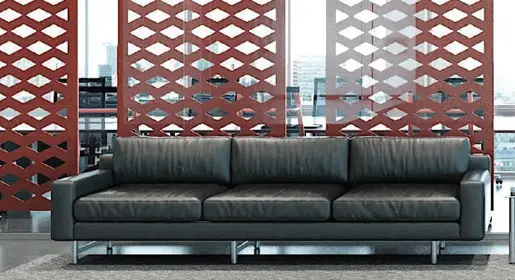 Hanging acoustic panels in dark red that function as room dividers forming semi-private meeting space behind with a modern black leather couch placed in front creating an more public space.