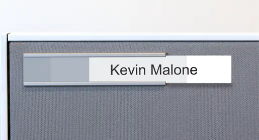 Frosted thin horizontal name panel with the name Kevin Malone attached to the gray panel of a workstation. Perfect for clear cubicle naming, wayfinding, and personalized branding in agile team environments.