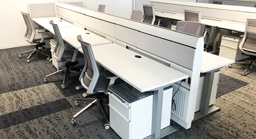 A pod of six grey and silver colored Knoll Currents workstations with box/file mobile storage. Grey task chairs pull up to each station.
