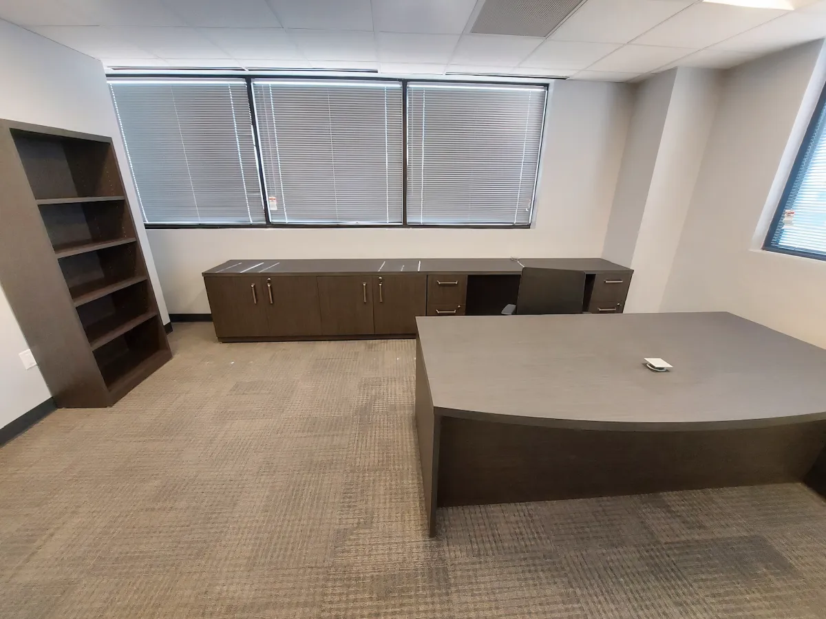 Spacious executive private office in OFC CONNECT series with large medium wood laminate curved desk, freestanding bookcase, low credenza storage, and natural light control blinds – innovative affordable modular office furniture from Office Furniture Connection Houston TX.