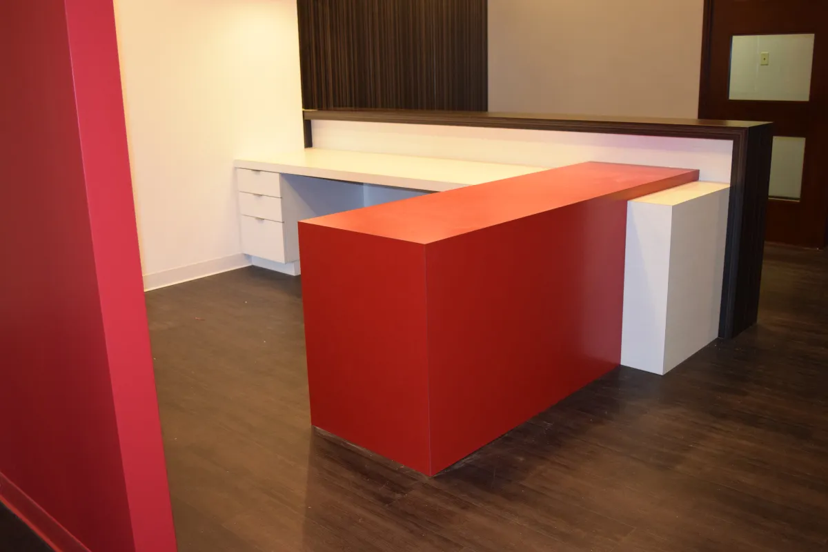Bold red, white, and dark wood laminate reception station from OFC CONNECT Series with floating transaction counter and integrated storage – dynamic modern lobby reception furniture custom crafted by Office Furniture Connection Houston TX.