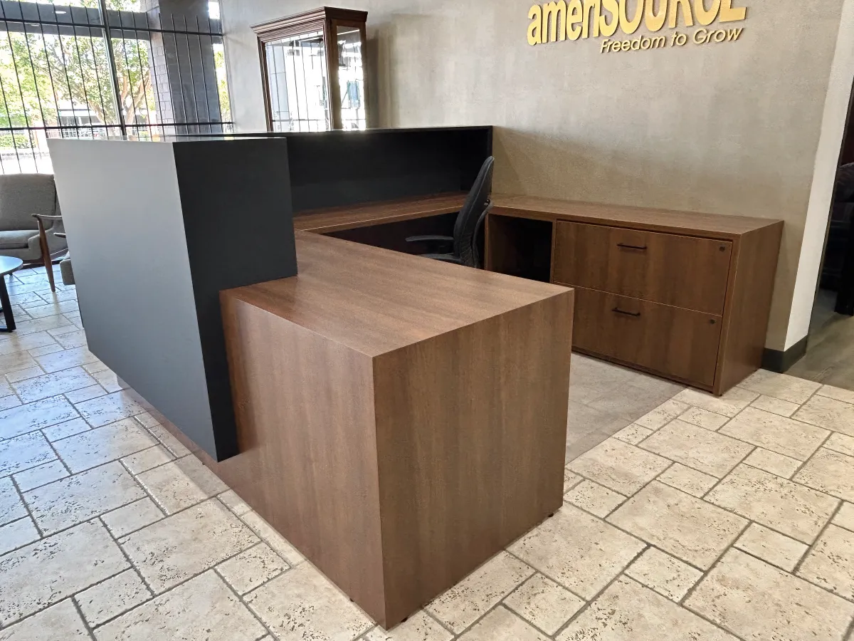 Warm walnut wood laminate U-shaped reception desk from OFC CONNECT Series with black accent riser, integrated storage credenza, and ergonomic task chair – professional affordable lobby greeting solutions by Office Furniture Connection Houston TX.