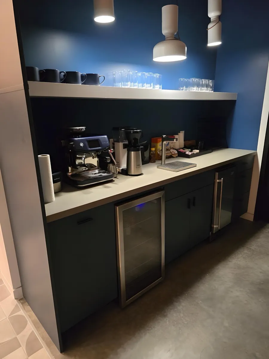 Navy blue premium coffee bar from OFC CONNECT Series with matte laminate cabinets, integrated beverage fridge, floating shelf, espresso machine station, and pendant lighting – luxury office kitchenette and breakroom storage solutions by Office Furniture Connection Houston TX.