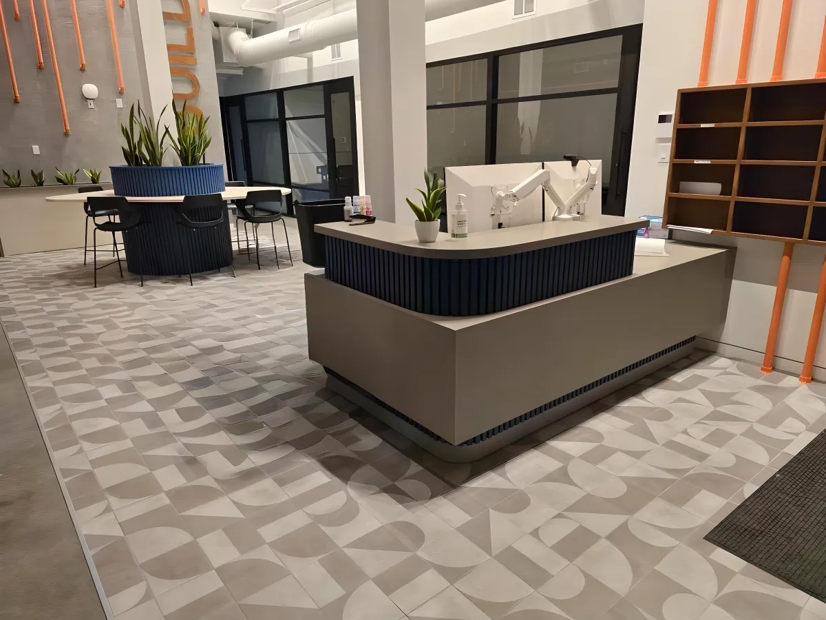 Contemporary reception and cafe area featuring OFC CONNECT Series two-tone reception desk, navy fluted planter table with black cafe chairs, and geometric tile floor – trendy collaborative lobby and breakroom solutions from Office Furniture Connection Houston TX.