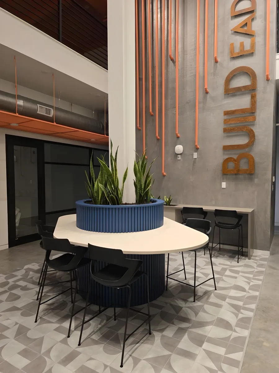 Unique, custom round cafe table with integrated blue fluted planter from OFC CONNECT Series surrounded by black modern stackable chairs and bold industrial decor – creative collaborative breakroom and lounge furniture by Office Furniture Connection Houston TX.