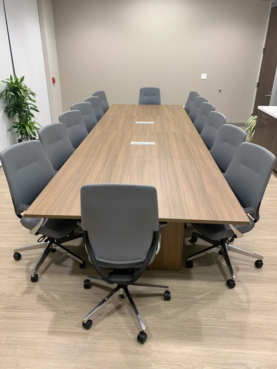 14-person rectangular conference table from OFC CONNECT Series in light oak wood laminate with dual power ports, 14 gray upholstered mid-back conference chairs, and clean contemporary styling – affordable collaborative meeting space solutions by Office Furniture Connection Houston TX.