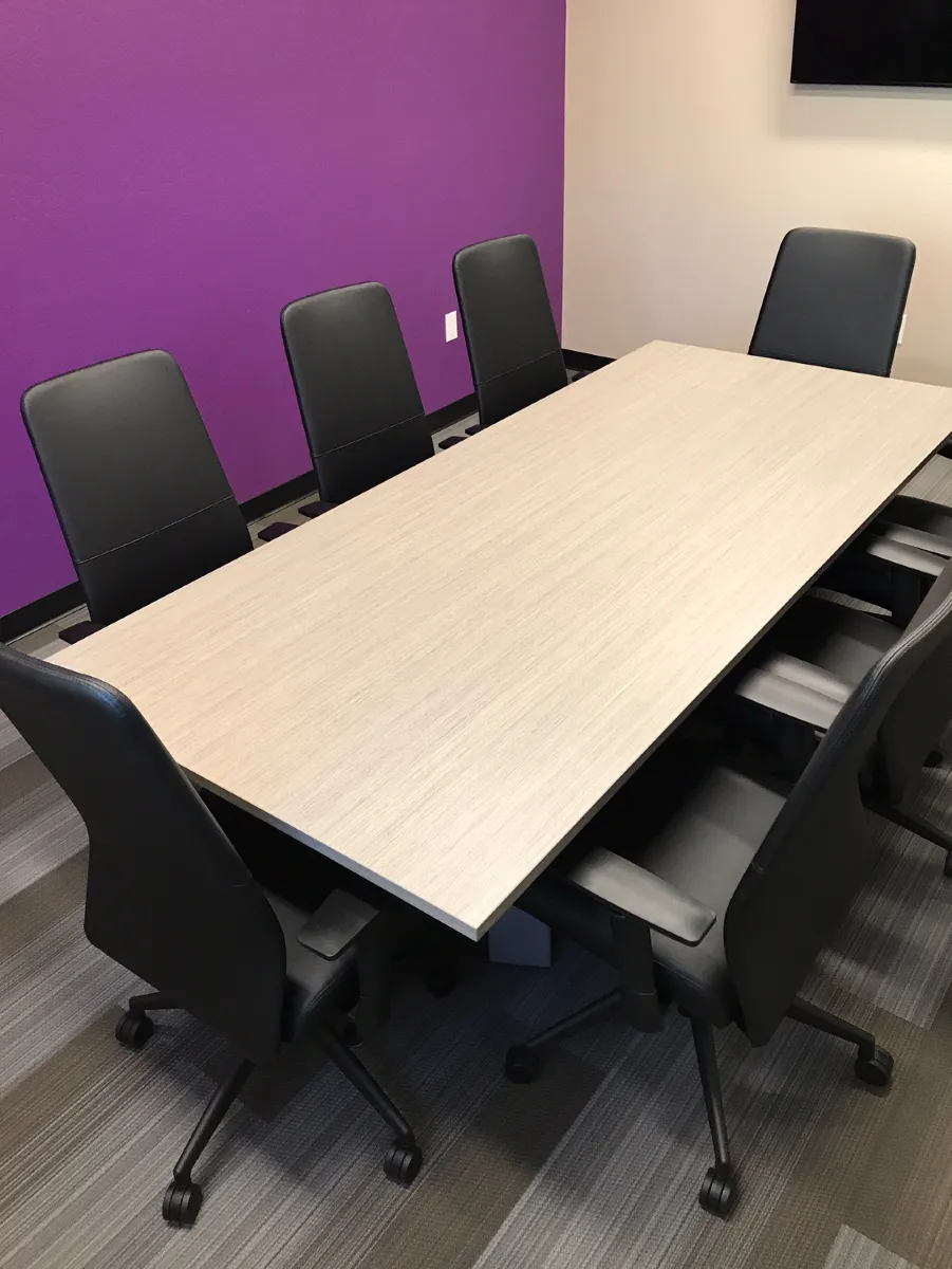10-foot racetrack conference table in light oak wood laminate from OFC CONNECT Series surrounded by black leather high-back executive chairs against vibrant purple accent wall – stylish professional boardroom seating packages by Office Furniture Connection Houston TX.