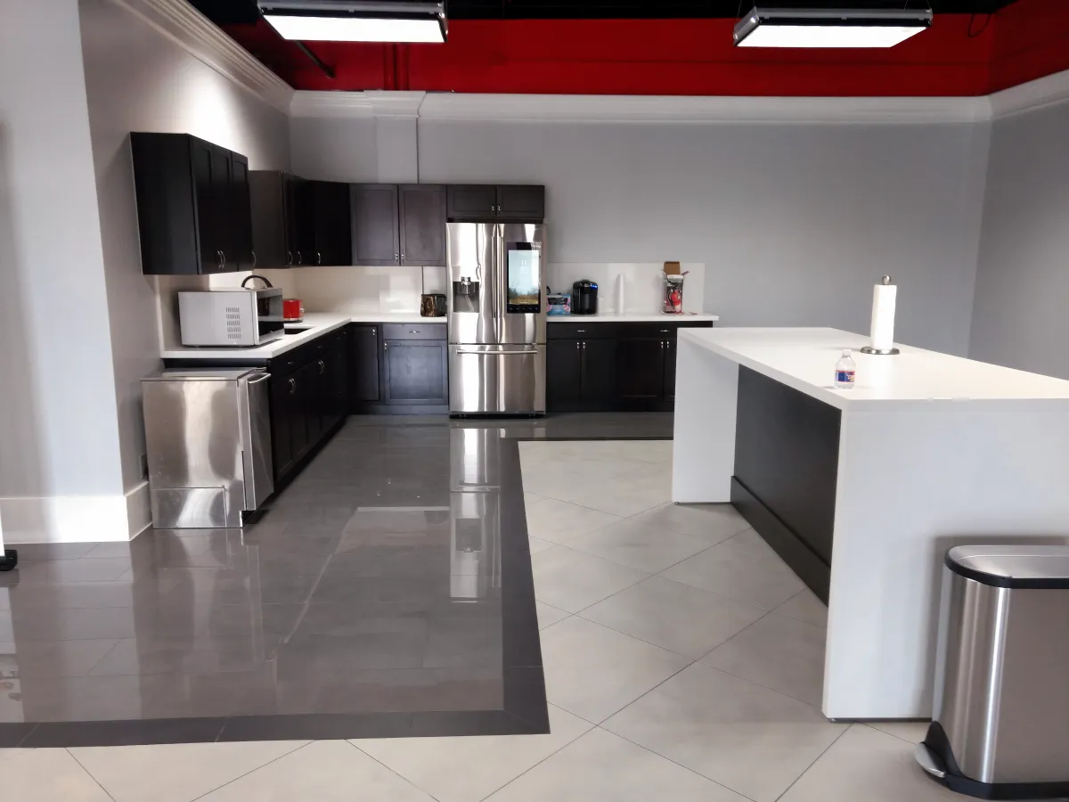 Sleek modern office breakroom kitchen from OFC CONNECT Series featuring dark espresso wood laminate cabinets, white countertops and collaboration island, and stainless appliances – complete employee cafe and lounge solutions by Office Furniture Connection Houston TX.