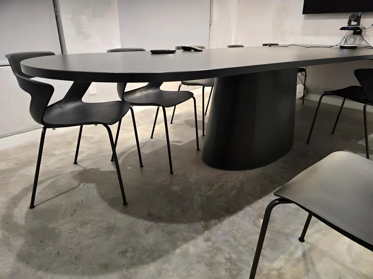 Modern matte black oval cafe/conference table from OFC CONNECT Series with tapered pedestal base, 8 sleek black stackable side chairs, and integrated power – contemporary breakroom and collaborative meeting table solutions by Office Furniture Connection Houston TX.
