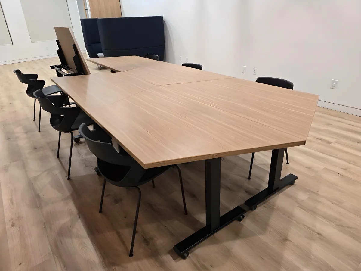 Unique hexagonal multi-purpose collaboration or training tables from OFC CONNECT Series in natural oak wood laminate with height-adjustable black metal bases and modern black cafe chairs – innovative modular team workspace and training table designs by Office Furniture Connection Houston TX.