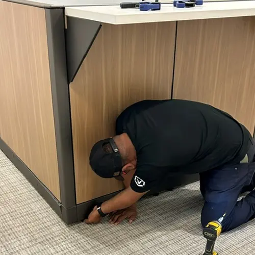 Knoll Morrison remanufactured wood-panel workstation installed by OFC skilled technician securing base trim and brackets using power tools for expert office furniture delivery and flawless on-site assembly.