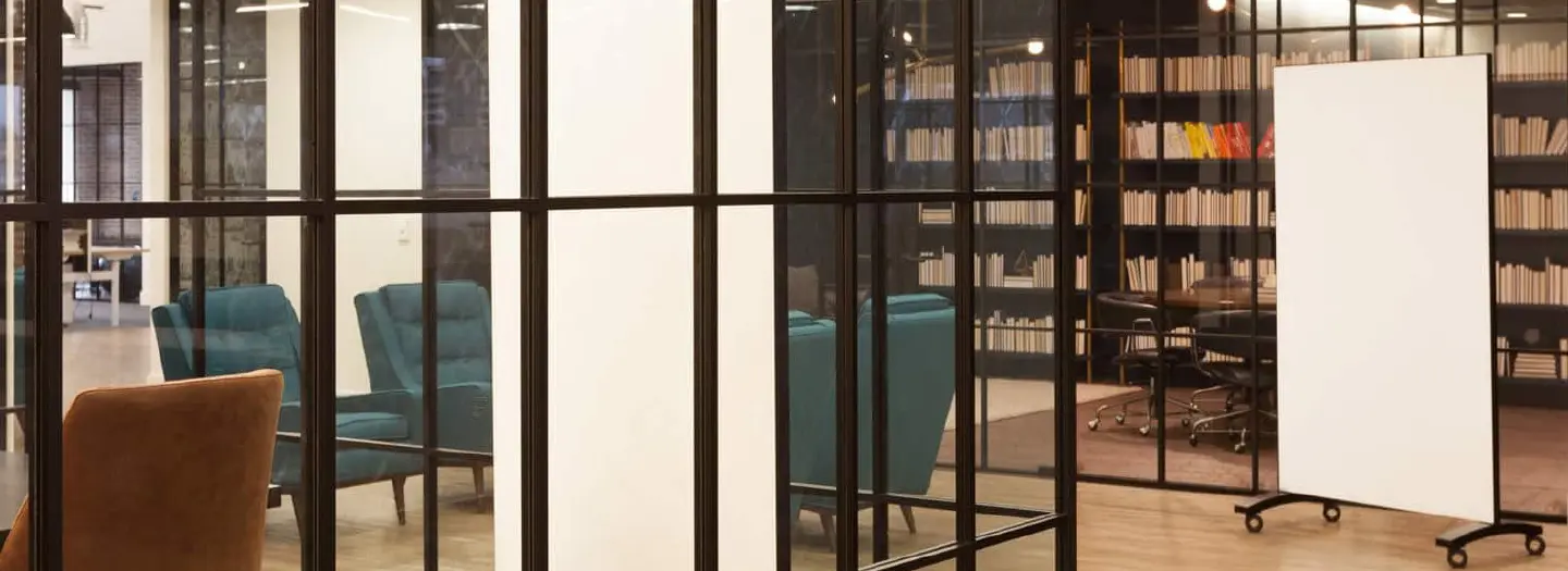 A large markerboard on wheels situated in a office enviroment ready to be wheeled into several meeting and conference areas.