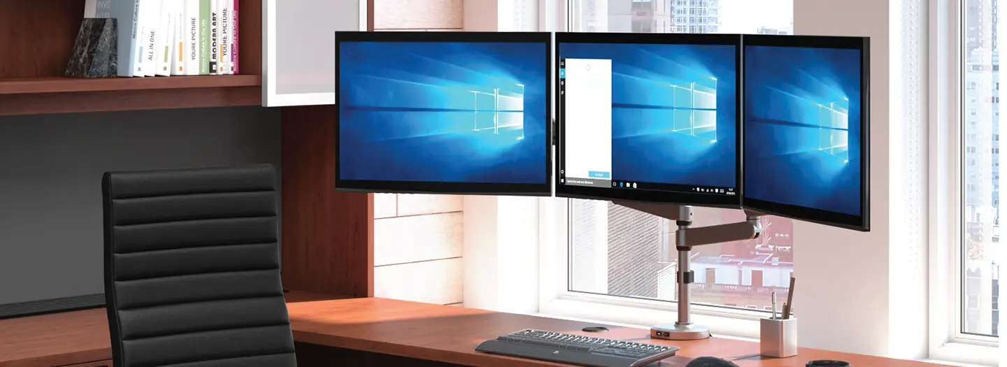 A monitor arm holding up three monitors on a wood transitional office desk
