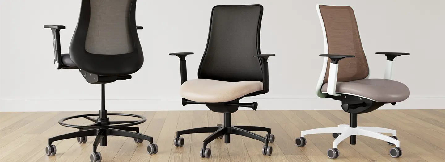 Three VIA ergonomic task chairs with adjustable arms and seat on casters. Seats are fabric and leather in neutral browns with black and white plastic and hardware.