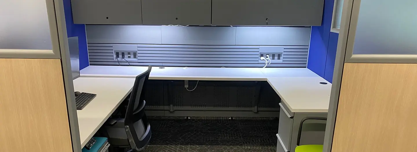 Knoll Morrison remanufactured cubicle with Knoll Currents spine fully supplied with worksurface height power and data. White worksurfaces in U-shape configuration with file/file pedestal, a blakc task chair and a guest chair with bright green fabric. Panels are a combination of bright blue fabric and wood laminate with locking grey overhead storage