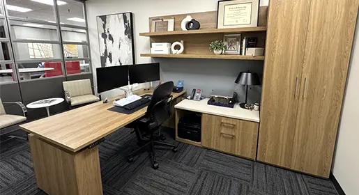 CONNECT series custom private office with sit stand desk, 2 drawer lateral file, open shelving and a wardrobe storage. A black Steelcase Leap task chair with two fabric and chrome guest chairs and small round side table. Two large monitors are attached to the worksurface with a dual monitor arm.