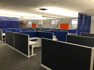 Remanufactured Knoll Morrison 6x6 cubicles with 42H blue/gray panels in a bright modern office with large windows, hanging perforated accoustic blue dividers, and orange accents. Perfect for open, collaborative team environments.