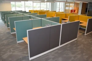 Colorful cluster of remanufactured Knoll Morrison workstations with teal, yellow, and gray 48H panels arranged in a bright, naturally lit office with large windows. Great for creative team environments.