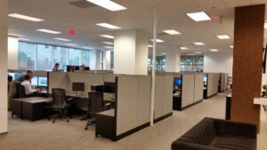 Employees collaborating in pods of remanufactured Knoll Morrison workstations powered through power poles to ceiling, 56"h beige panels with dark trim and free-standing lateral files, black ergnomic task chairs benefitting from the ability to have focused work time or space to interact with others.