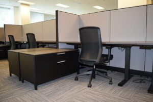 Cloves up of previous remanufactured Knoll Morrison workstations with 56"h beige panels with dark trim, dark wood tone laminate adjustable height worksurfaces, and free-standing lateral files, and black ergnomic task chairs for employee comfort