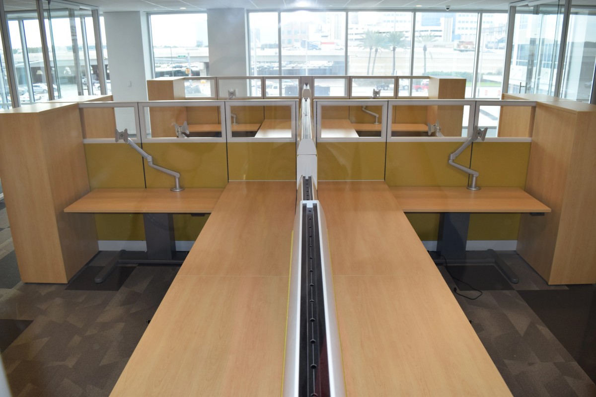 Remanufactured Knoll Morrison workstations with Currents spine providing worksurface power and data; wood laminate surfaces, electric height-adjustable desks, monitor arms, and wood wardrobe storage at end of each station.