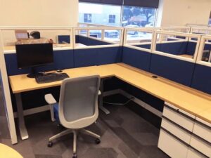 Remanufactured 6x8 office cubicles with 56"H blue fabric panels, glass stackers, height-adjustable light tone wood laminate desks, box/box/file pedstal, and grey task chair in a bright office. Ideal for call centers or open-plan offices.