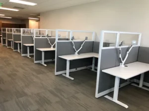 Row of remanufactured Knoll Morrison open workstations with 48"h gray fabric and 16"h glass panels, white adjustable height desk with return along a wall to maximize space for employees.