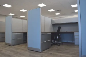 Row of remanufactured Knoll Morrison cubicles with 64"h blue and gray panels, wood-tone worksurfaces, overhead lockable storage with task light, lateral filing, and ergonomic chairs on wood-look flooring.