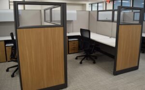 Two remanufactured Knoll Morrison workstations with 64" beige fabric panels with 16" glass at top and wood laminate return panels, white L-shaped worksurface with grommets, overhead storage, wood front lateral file and upholstered mobile box/file, refurbished and black Haworth Zody task chair.