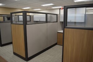 Row of remanufactured Knoll Morrison workstations with 64" beigefabric panels with 16" glass at top and wood laminate return panels, white worksurfaces, gray overhead storage, and wood front lateral file for an upscale office vibe.