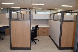 Remanufactured Knoll Morrison workstations in side view with 64" beige fabric panels with 16" glass at top and wood laminate return panels, white L-shaped worksurface with grommets, overhead lockable storage, wood front lateral file and upholstered mobile box/file, and refurbished and black Haworth Zody task chair for focused yet open area work.