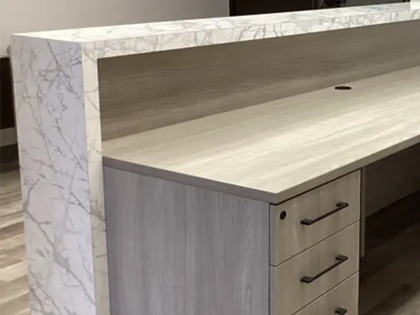 A reception desk with a marble laminate counter and gray wood laminate worksurfaces and box/box/file storage