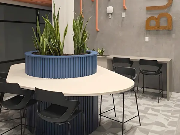 A tall blue round planter and bar height organic shaped worksurface built around a column in a commercial office space