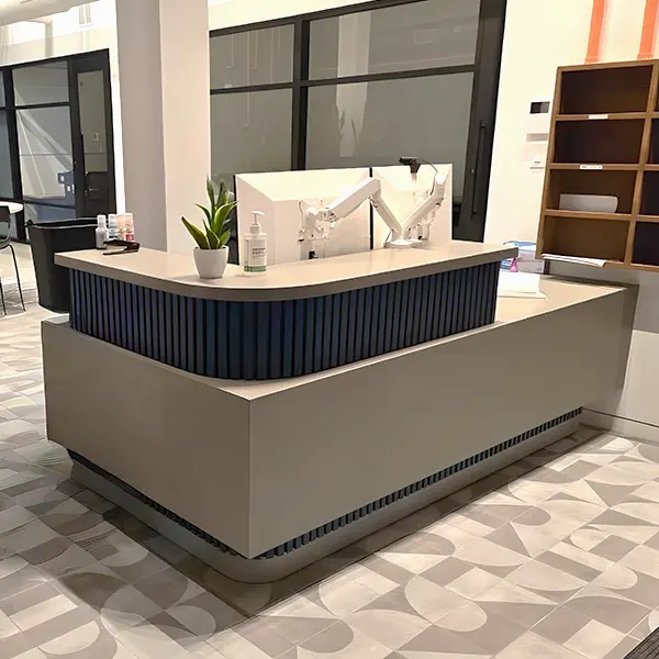 New CONNECT series curved reception desk with dual monitor arms, small potted plant, hand sanitizer, and blue accent paneling in contemporary lobby with patterned tile – new reception counters and welcome desks for sale Houston TX at Office Furniture Connection.