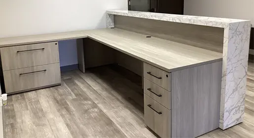 A custom CONNECT series reception desk with marble style laminate used as the counter worksurfaces. The reception workspace is a grey wood laminate with black hardware. Storage consistes of a two drawer lateral file and a box/box/file.