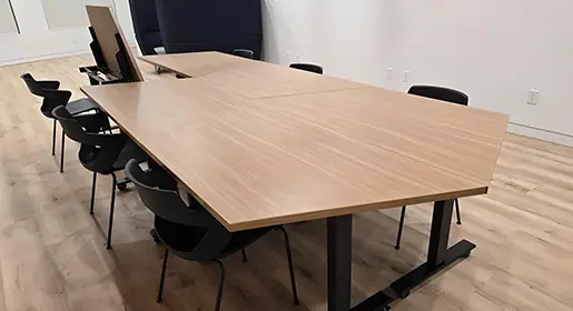 A conference room with CONNECT Custom conference or training tables with medium wood laminate flip tops and modern black training chairs.