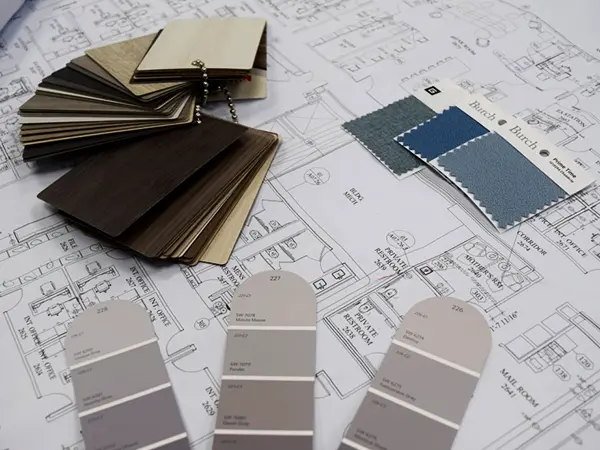 Detailed office space planning session with architectural floorplans, wood finish samples, fabric swatches and paint colors – expert designers optimizing layouts using high-quality diverted office furniture to reduce waste and cost.