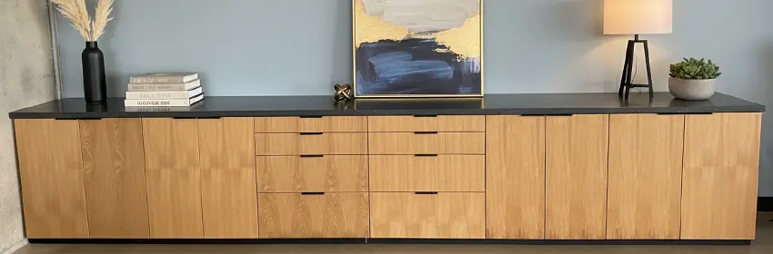 CONNECT series 20-foot credenza with closed storage and drawers, dark stone top decorated wtih a small lamp, plant, books and artwork in front of a light blue painted wall. Customed designed and built for Concrete Reinforements, Inc.