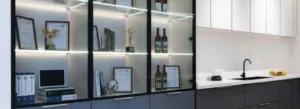 Elegant black-framed glass display cabinet with integrated LED shelf strip lighting showcasing trophies, awards, and wine bottles – luxury executive office accent illumination by Office Furniture Connection Houston TX.