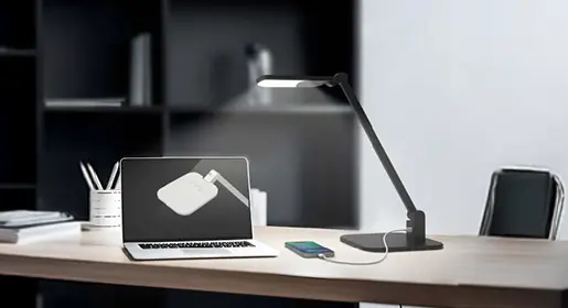 Sleek matte black adjustable LED task lamp with built-in USB charging port and wireless phone charger illuminating laptop workstation – high-performance modern desk lighting from Office Furniture Connection Houston TX.