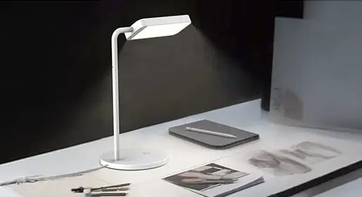 Modern white LED desk task light with sleek curved arm, touch controls, and focused illumination on workspace with laptop and notebook – premium ergonomic office lighting solutions from Office Furniture Connection Houston TX.