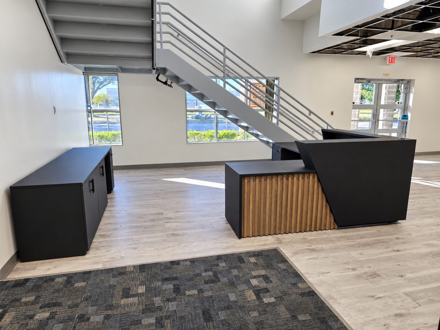 Custom black reception desk with wood slats and matching credenza in a lobby beneath a staircase